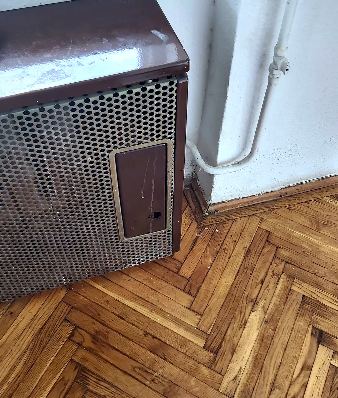 Barna gázkonvektor parkettás szobában, az ablak alatt
