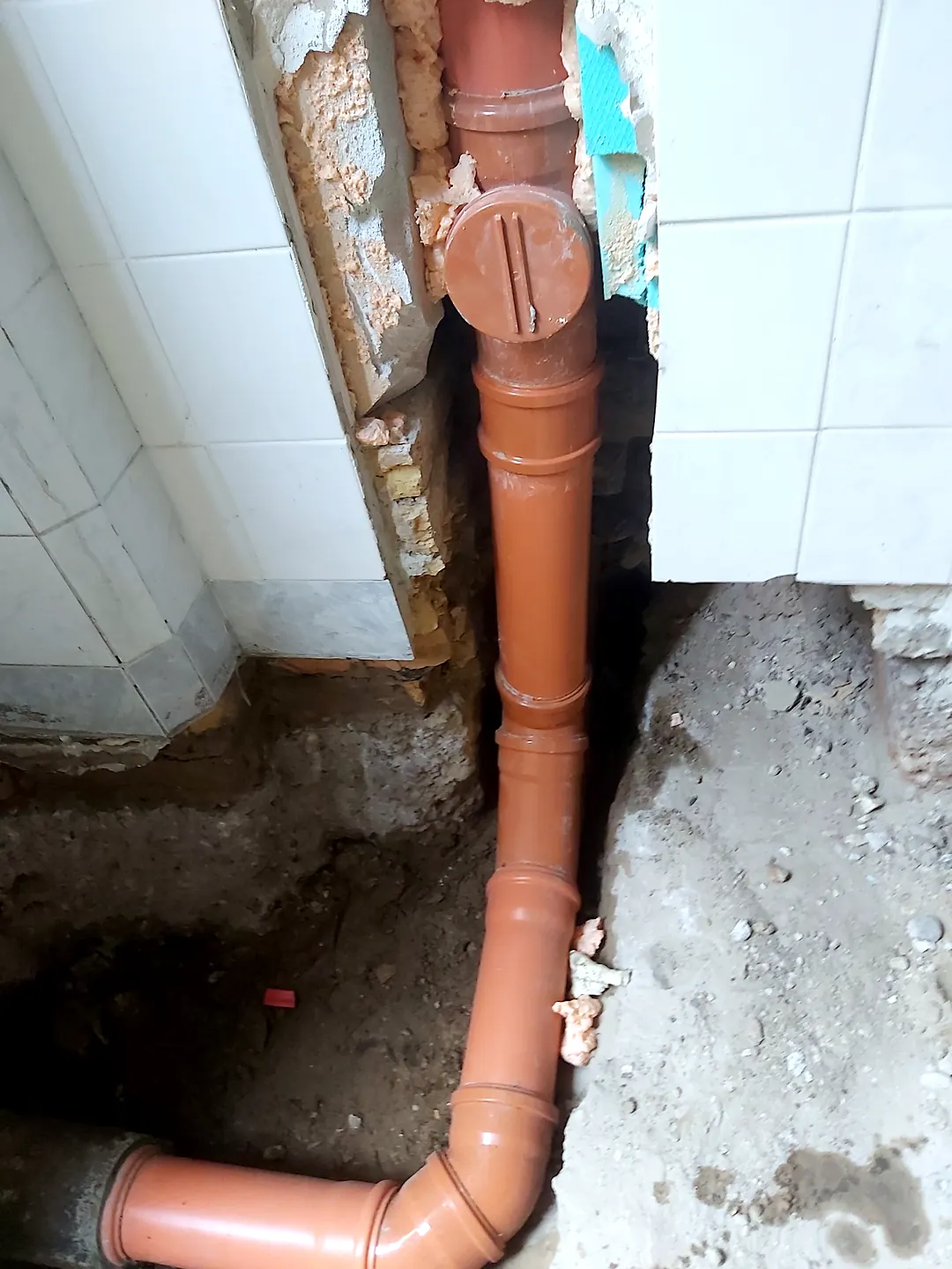 Narancssárga lefolyócső függőlegesen a falban, a csempe mellett